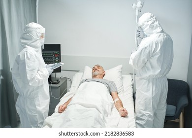 Two Medical Specialists Wearing Personal Protection Equipment Working With Patient In Infectious Disease Department