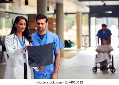 Two Medical Staff In White Coats And Scrubs With Patient Scans Having Informal Meeting In Hospital - Powered by Shutterstock