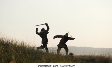 Two medieval warriors Viking are fighting with swords and shields in the meadow. Medieval Reenactment. Contre-jour