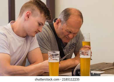 Two men adult son and senior father drinking light beer, cheering together and having a discussion on czech pub terrace in the summer weekend. Best friends. Family and Father's Day celebration concept