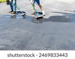 Two men applying sealer on asphalt driveway with brush and squeegee on sunny day