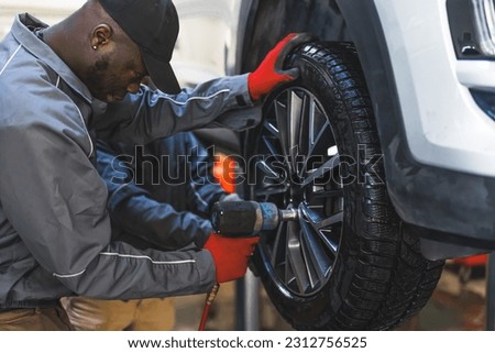 Two men auto mechanics changing car tire on a vehicle on a hoist using an electric drill to loosen the bolts . High quality photo