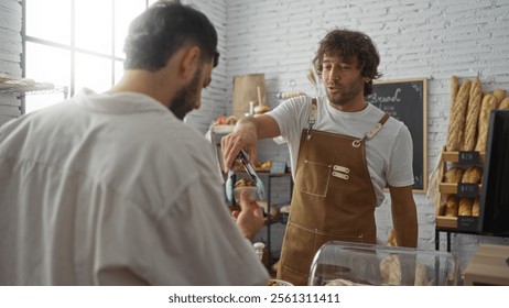 Two men in a bakery with one serving as a baker and the other as a customer, exchanging baked goods in an indoor shop setting.