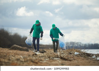 Two men with big sacks walking along river bank, picking up litter and putting it in those sacks - Powered by Shutterstock