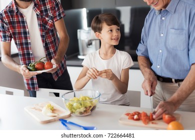 Two Men And A Boy Prepare A Salad For Thanksgiving. The Boy Tears The Leaves Of The Salad, The Old Man Cuts The Tomatoes, The Man Brought More Vegetables To The Salad