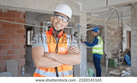 Two men builders standing with arms crossed gesture working at construction site