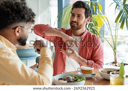Two men conversing at a cafe table, one actively signing, sharing a meal and coffee during a friendly meeting