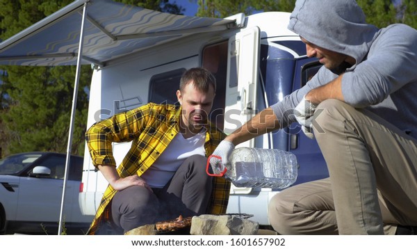 Two men cook meat on the grill near the
campervans in nature.