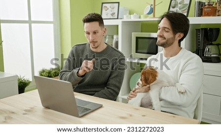 Two men couple using laptop sitting on table with dog at dinning room