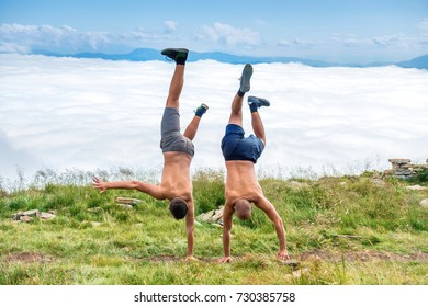 Two men dancing and making acrobatic tricks on green grass with white clouds on background