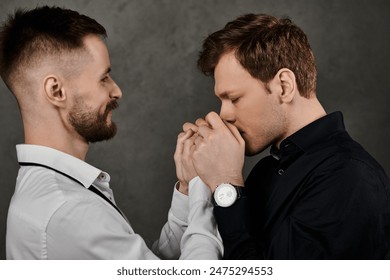 Two men in dapper suits share a loving moment, holding hands and looking at each other.