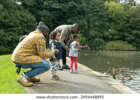 Two men with daughters looking at ducks on pond in park