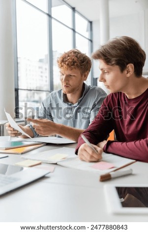 Two men deep in study, papers and pens scattered on the table.