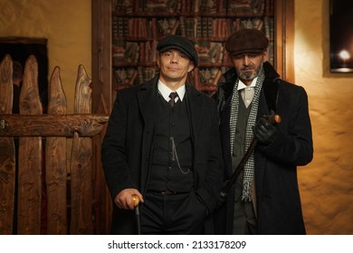 Two men of different ages, English retro gangster of the 1920s dressed in a coat, suit and flat cap in Peaky blinders style.