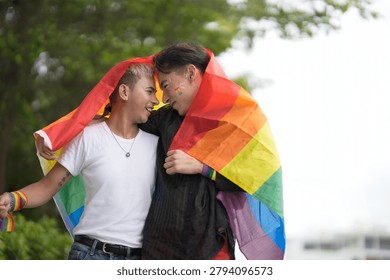 Two men embracing affectionately while wrapped in a vibrant rainbow flag, symbolizing love and pride during an outdoor celebration