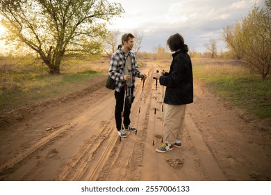 Two men engage in conversation while hiking on a sandy path surrounded by trees during a beautiful sunset - Powered by Shutterstock