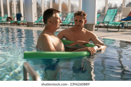 Two men engaged in conversation during aquatic rehab with pool noodles