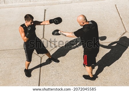 Two men exercising and fighting in outside. Boxer in gloves is training with a coach