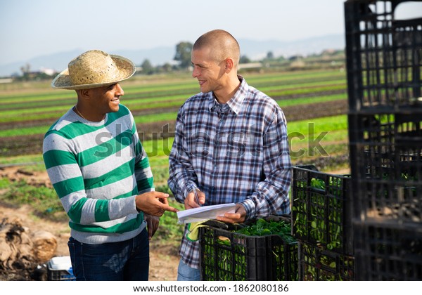 Two men farmers discussing and signing papers on\
vegetables farm