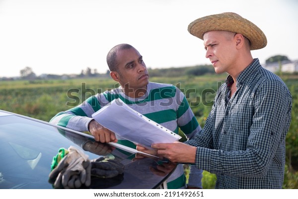 Two men farmers discussing and signing papers near\
car on farm