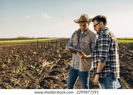 Two men farmers standing in the field and looking at the tablet