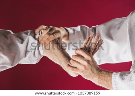 Two men fighting at Aikido training in martial arts school. Healthy lifestyle and sports concept. Men in white kimono on red background. Male hands closeup on red studio background