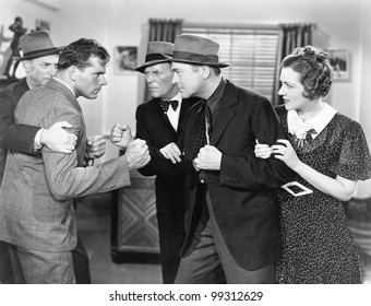 Two Men Fighting With Each Other And Being Held Back By A Woman And A Man