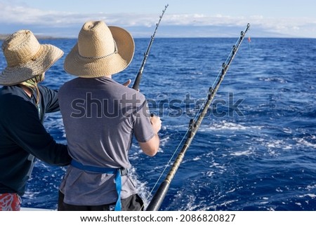 Two men fishing on a boat. Fishing trip while on vacation. Deep blue water, nice sky. 