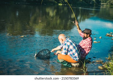 Two Men Friends Fishing. Flyfishing Angler Makes Cast, Standing In River Water. Old And Young Fisherman. Catching Trout Fish.