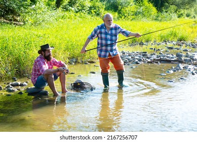 Two Men Friends Fishing. Flyfishing Angler Makes Cast, Standing In River Water. Old And Young Fisherman.