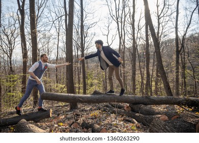 Two Men, Gay Couple Holding Hands, Walking In Woods With Their Dog, Helping Each Other Cross A Log.