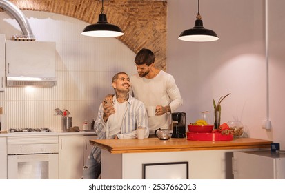 Two men, a gay couple, are spending quality time together in their modern kitchen, enjoying a morning coffee while one of them shows something interesting on his smartphone - Powered by Shutterstock