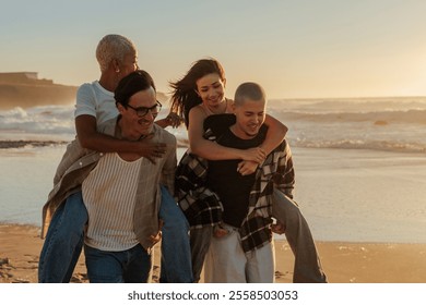 Two men giving piggyback rides to their female friends while walking on the beach at sunset - Powered by Shutterstock