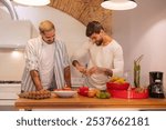 Two men happily cooking together in a modern kitchen, bonding over food and sharing intimate moments. Tattooed arms chopping veggies and cracking eggs