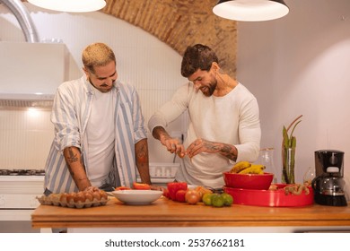 Two men happily cooking together in a modern kitchen, bonding over food and sharing intimate moments. Tattooed arms chopping veggies and cracking eggs - Powered by Shutterstock