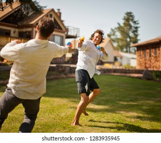 Two Men Having A Water Gun Fight In A Backyard.