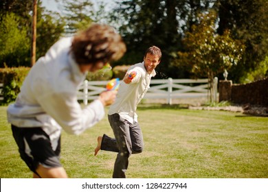 Two Men Having A Water Gun Fight In A Backyard.