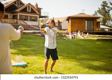 Two Men Having A Water Gun Fight In A Backyard.