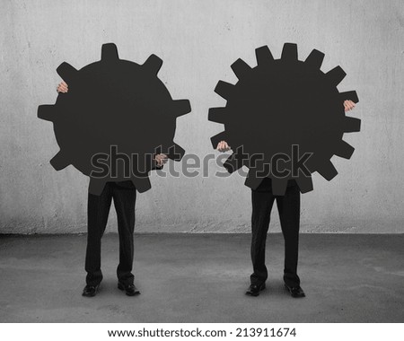 two men holding their different gear on concrete floor with cement wall