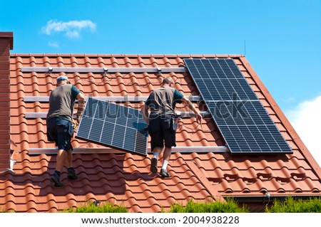 Two men installing new solar panels on the roof of a private house. Renewable energy concept and green energy abstract. Foto stock © 