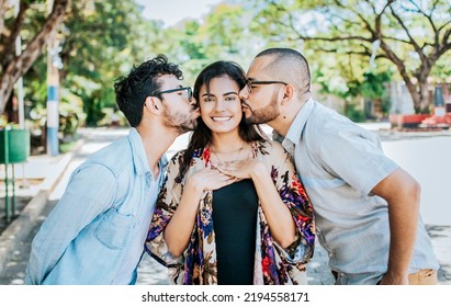 Two Men Kissing A Girl Cheek. Portrait Of Two Guys Kissing A Girl Cheek. Two Young Men Kissing A Woman Cheek Outdoor, Love Triangle Concept. Polygamy Concept