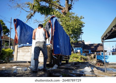 Two men load large blocks of ice onto the back of a truck. The setting appears tropical and the day is bright.