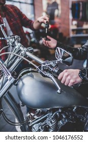 Two Men In Motorcycle Shop. Customer And Salesman. Shop Assistant Is Helping Bearded Man In Choosing New Vehicle, Motorcycle Accessories And Other Biker Stuff. Giving Keys To New Owner.