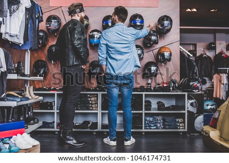 Two men in motorcycle shop. Customer and salesman. Shop assistant is helping bearded man in choosing new vehicle, motorcycle accessories and other biker stuff. Buying new helmet.Safety driving concept