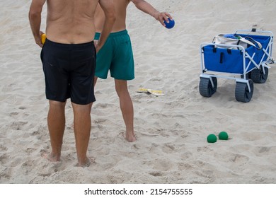 Two Men On The Beach Playing Bocci Ball With A Blue Beach Cart