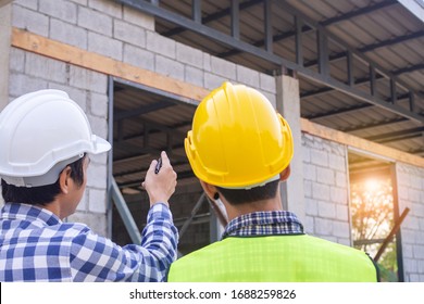 Two men on construction site wearing hard hats. Standing and talking about the problems of house construction.