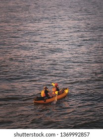 Two Men Paddling A Kayak In A Colourful Sunset Over Hudson River, New York With The New Jersey City Skyline In The Background