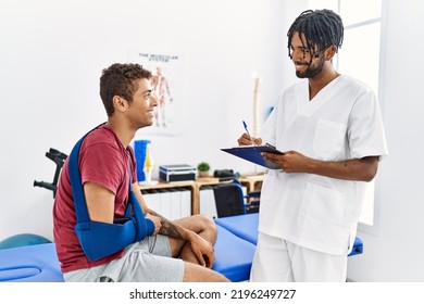 Two Men Physiptherapist And Patient Having Rehab Session Writing Accident Report At Clinic