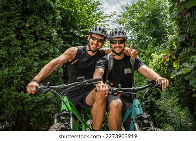 two men portrait of caucasian friends male standing in front of electric bikes e-bike while taking a brake outdoor ride in sunny summer day wear protective helmet