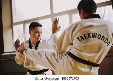 Two men practicing taekwondo together in the gym. People stand in the hall and practice martial arts techniques. 